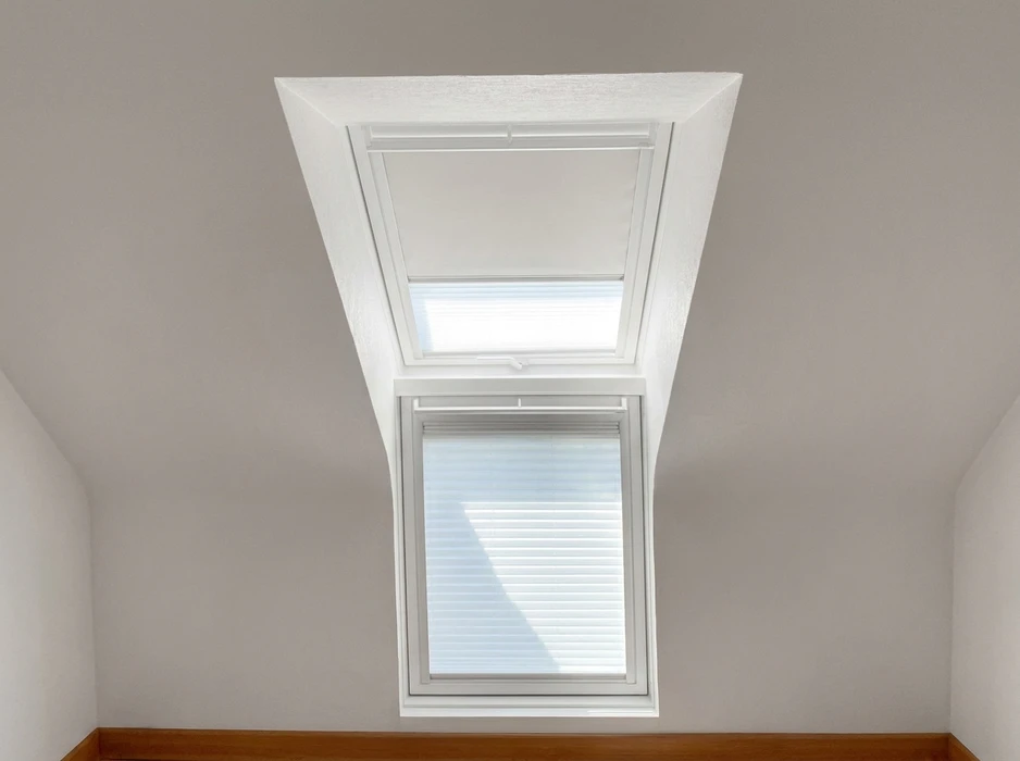 Vue intérieure en contre-plongée d'une fenêtre de toit double corps avec store plissé blanc partiellement déployé