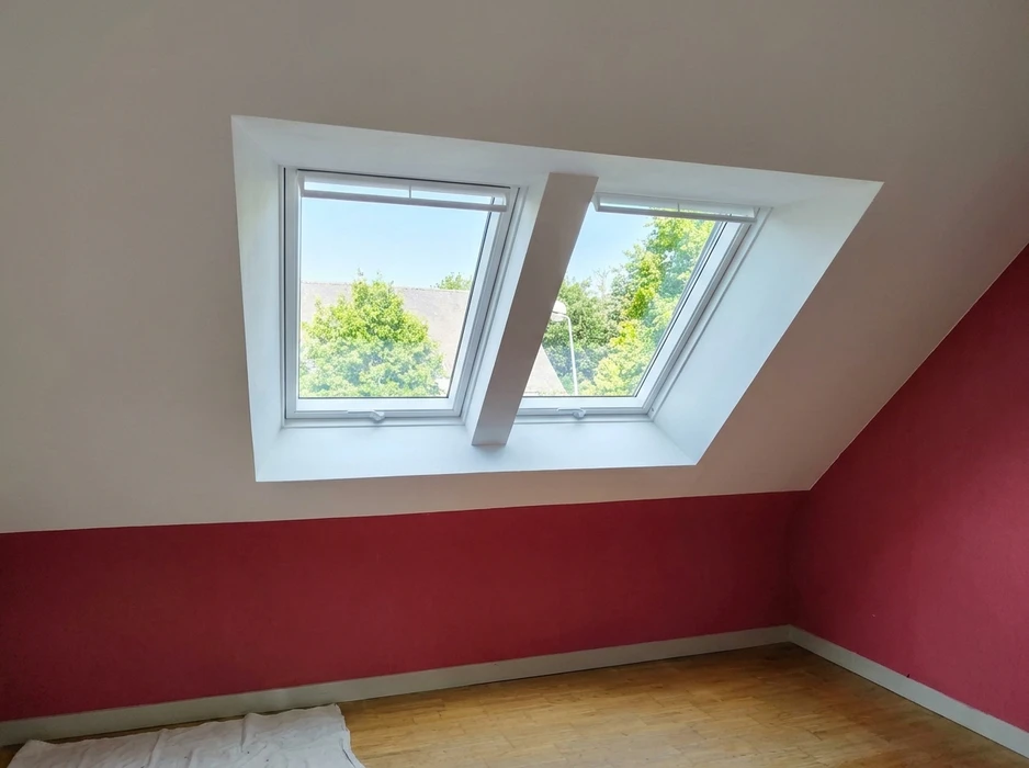 Chambre mansardée avec deux fenêtres de toit VELUX côte à côte, encadrées de boiseries blanches sur mur incliné