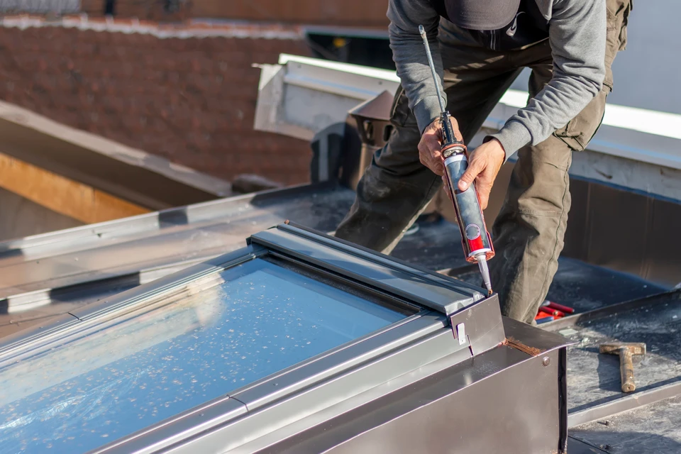Un homme installe un film plastique de protection autour d'un châssis de fenêtre de toit Velux dans des combles en construction