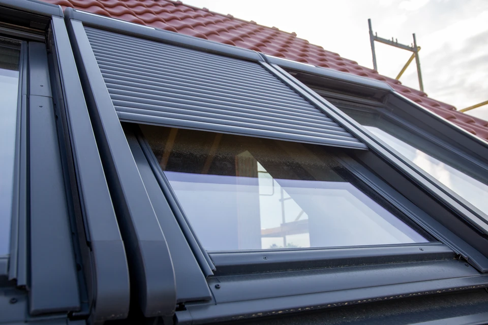 Un homme installe un film plastique de protection autour d'un châssis de fenêtre de toit Velux dans des combles en construction